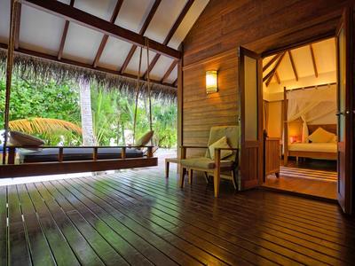 Offene Holzveranda mit Stuhl und Hängematte vor einem Schlafzimmer in luxuriösem Bungalow.