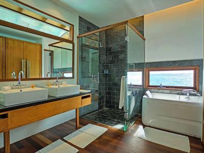 Moderní koupelna s dvojitými umyvadly, skleněným sprchovým koutem a vanou s výhledem na moře.