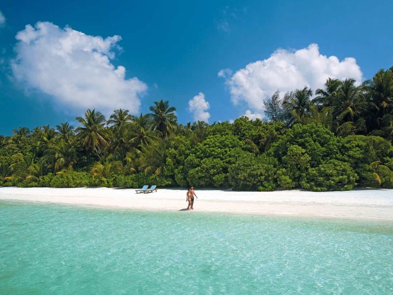 Pláž s bílým pískem, tyrkysovou vodou a hustou tropickou vegetací v pozadí.