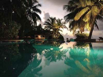 Piscina illuminata di notte con palme e vista sul mare