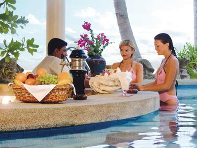 Tre persone sedute al bar in piscina con decorazioni tropicali.