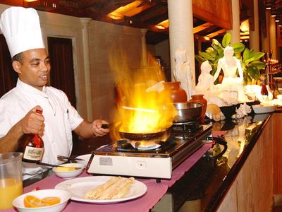 Cuoco in uniforme bianca prepara un piatto flambé alla postazione di cucina nel ristorante.
