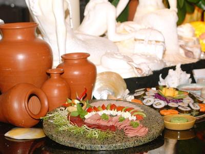 Piatto con cibo disposto artisticamente e anfore di terracotta su un tavolo con sculture bianche sullo sfondo