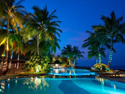 Beleuchteter Pool mit Palmen bei Nacht in tropical Hotelanlage.