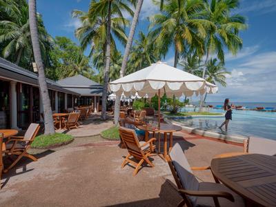 Poolbereich eines Hotels mit Sonnenschirmen, Liegestühlen und Palmen am Meer