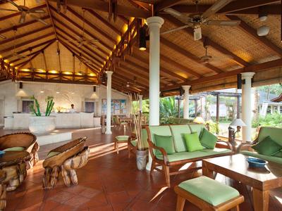 Un lounge tropicale aperto dell'hotel con mobili in legno e vista sulla vegetazione lussureggiante.