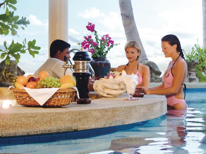 Tre persone sedute al bar in piscina con decorazioni tropicali.