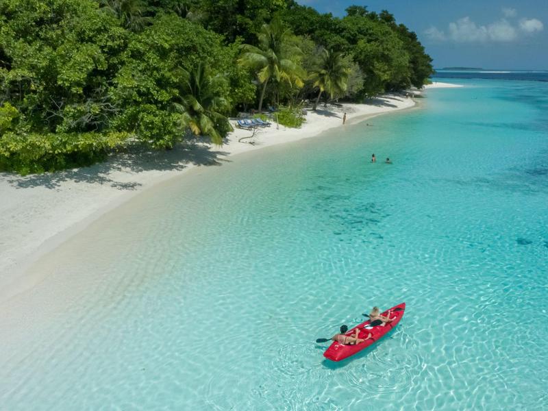 Kayak rosso su acqua turchese limpida vicino a spiaggia di sabbia bianca e vegetazione verde.