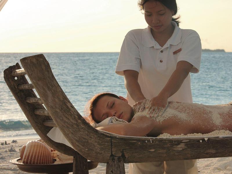 Donna che riceve un massaggio sulla spiaggia con vista sul mare al tramonto.