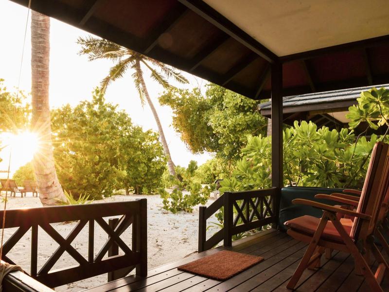 Veranda con sedie in legno che si affaccia su alberi tropicali al tramonto.