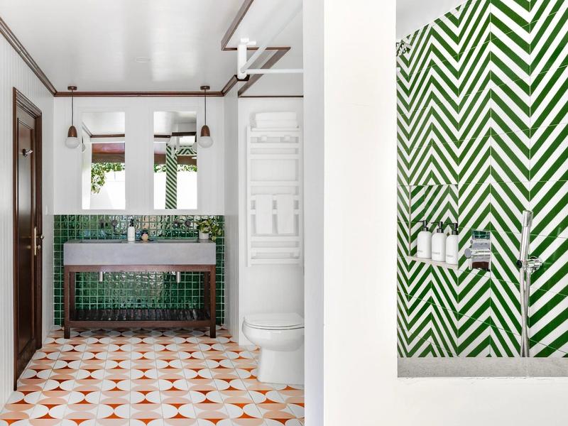 Bagno luminoso con piastrelle verdi e pavimento geometrico in una camera d'hotel.