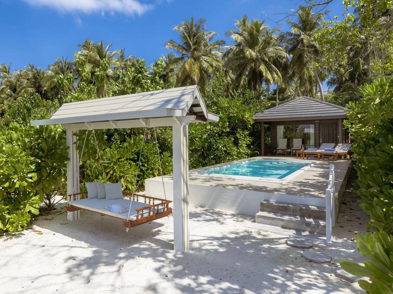 Amaca moderna con tettoia accanto a una piscina e un padiglione in un giardino tropicale.