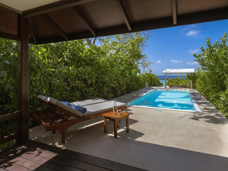 Terrazza coperta con lettino e tavolo, vista sulla piscina privata e mare sullo sfondo.