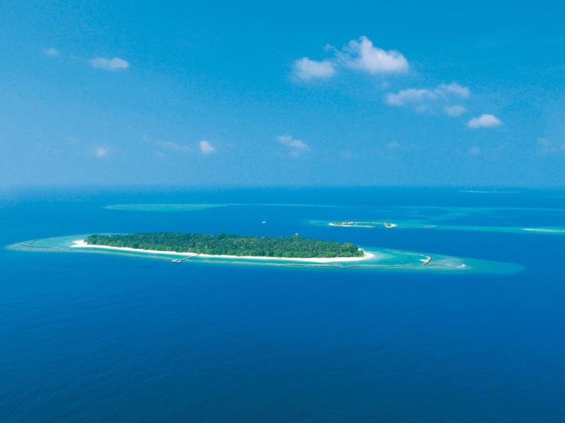 Piccola isola tropicale con vegetazione verde, circondata da acqua turchese e cielo limpido.