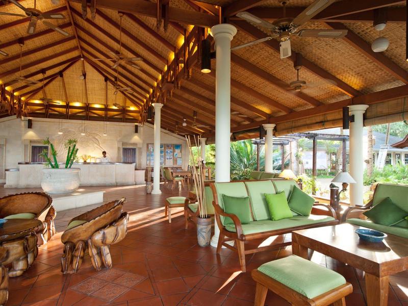 Un lounge tropicale aperto dell'hotel con mobili in legno e vista sulla vegetazione lussureggiante.