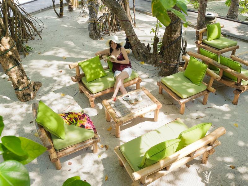 Persona rilassata seduta su divano in legno con cuscini verdi all'aperto sotto palme.