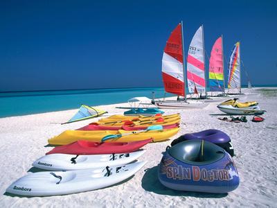 Reihe bunter Segelboote und Surfbretter am weißen Sandstrand bei klarem blauem Himmel