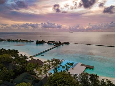 Luxuriöse Overwater-Bungalows an einem Steg über dem türkisfarbenen Meer bei Sonnenuntergang.