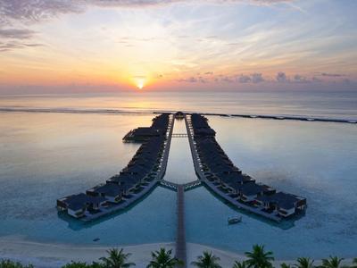 Sonnenuntergang über einer Wasseranlage mit zwei langen Stegen und Bungalows im Meer