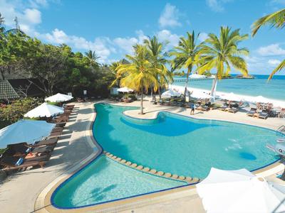 Poolbereich mit Liegestühlen, Palmen und Blick auf den Strand und das Meer.