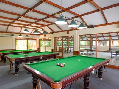 Ein geräumiger Billardraum mit zwei grünen Billardtischen und großen Fenstern.