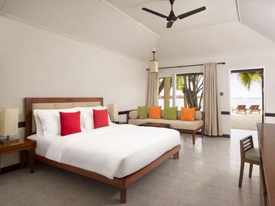 Helles Schlafzimmer mit großem Bett, bunten Kissen, Sofa, Ventilator und Terrasse mit Liegestühlen.