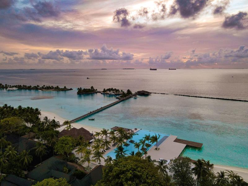 Luxuriöse Overwater-Bungalows an einem Steg über dem türkisfarbenen Meer bei Sonnenuntergang.
