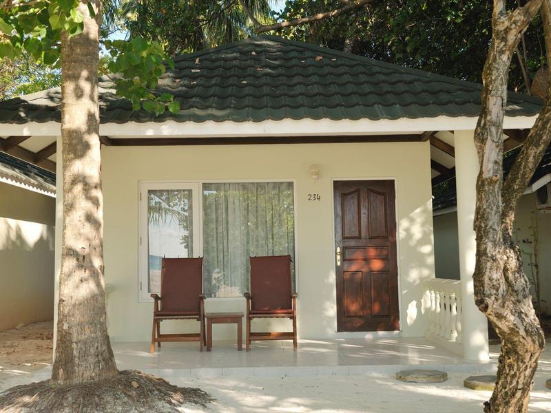 Kleines Ferienhaus mit zwei Stühlen vor der Tür, umgeben von Bäumen.