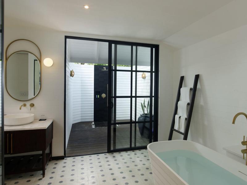 Helles Badezimmer mit freistehender Badewanne, runder Spiegel und geteilten Glastüren.