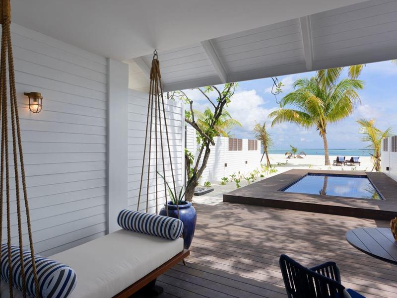 Überdachte Terrasse mit Hängematte und Blick auf einen Pool und Palmen am Strand
