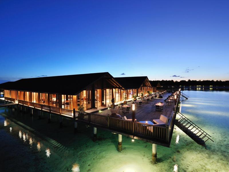 Luxuriöse Überwasserbungalows beleuchtet bei Nacht mit Blick auf das ruhige Meer.