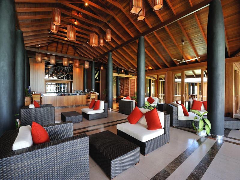 Modern eingerichteter Hotel-Lounge-Bereich mit Rattanmöbeln, Kissen und Holzdach.