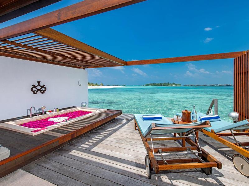 Offene Terrasse mit Außendusche, Liegestühlen und Blick auf türkisfarbenes Meer bei klarem Himmel.