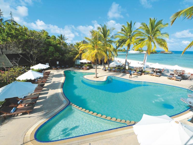 Poolbereich mit Liegestühlen, Palmen und Blick auf den Strand und das Meer.