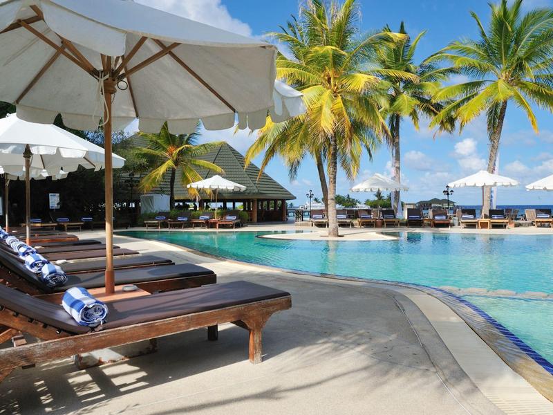 Poolbereich mit Liegestühlen, Sonnenschirmen und Palmen an einem sonnigen Tag