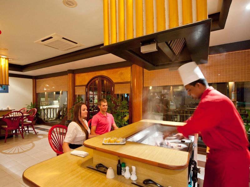 Koch in roter Uniform bereitet Speisen an einem Teppanyaki-Grill in einem Restaurant zu