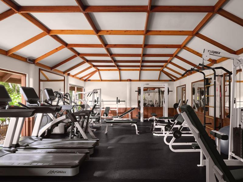 Moderne Fitnessstudiohalle mit Holzdecke, Laufbändern, Kraftgeräten und Spiegelwand.