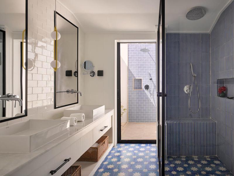 Helles Badezimmer mit Doppelwaschbecken, großen Spiegeln, blauen Fliesen und Walk-In-Dusche.