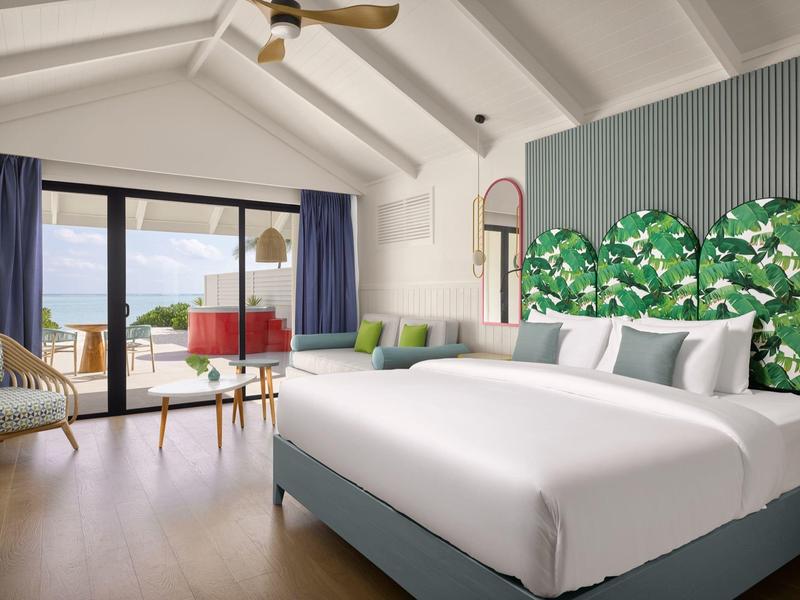 Modernes Schlafzimmer mit großem Bett, grün gemustertem Kopfteil und Meerblick durch Glasschiebefenster.