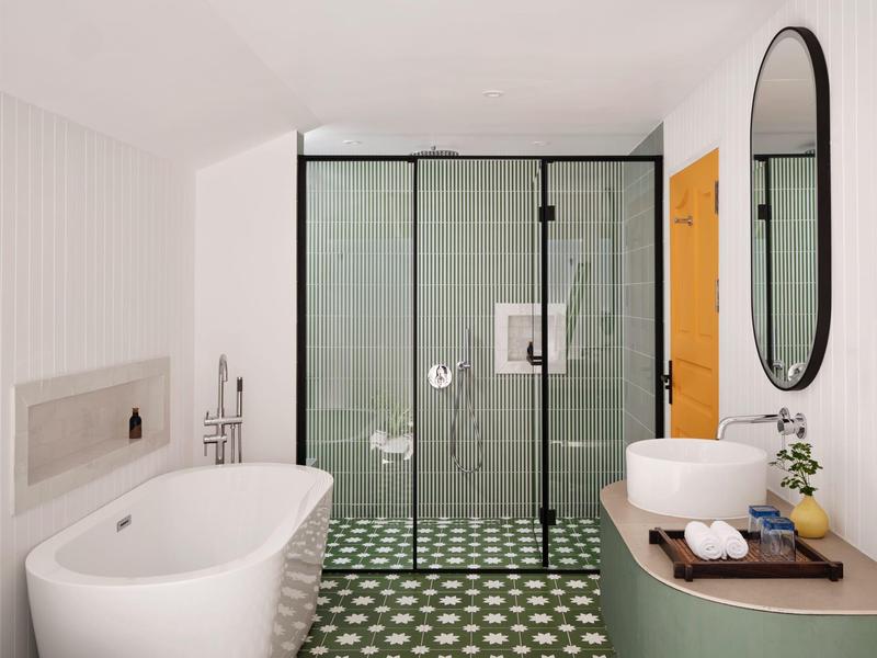 Helles Bad mit freistehender Badewanne, Glasdusche, rundem Spiegel und hellgrünem Farbton.