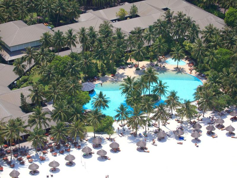 Vogelperspektive eines tropischen Pools umgeben von Palmen und Sonnenschirmen am Strand.