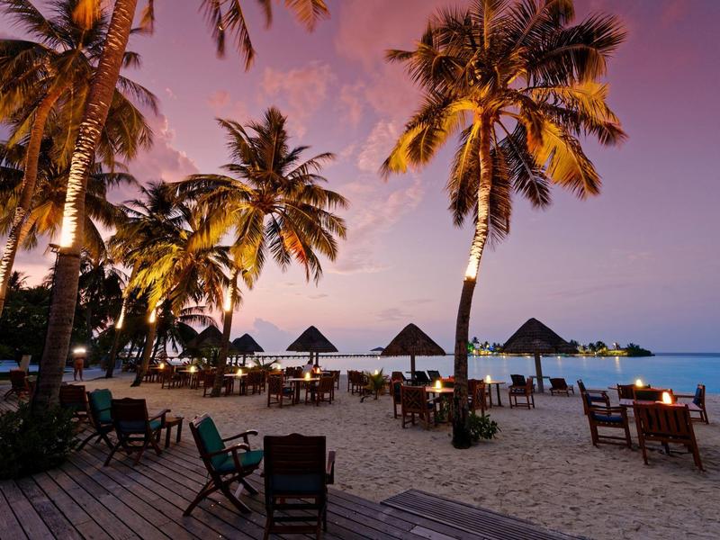 Strandrestaurant mit Tischen und Stühlen unter Palmen bei Sonnenuntergang