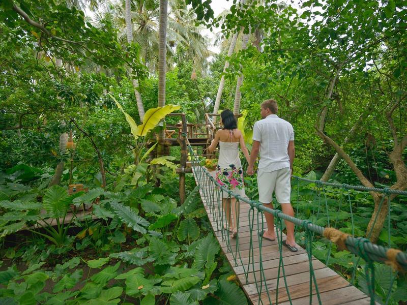Paar läuft barfuß über eine Hängebrücke im tropischen Dschungel.