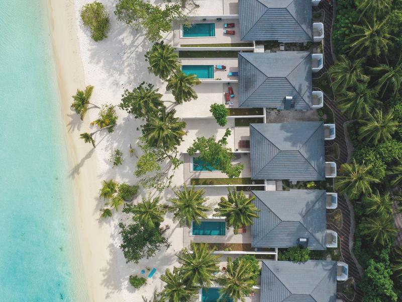 Vogelperspektive auf Strandvillen mit Pools neben einem türkisfarbenen Meer und Palmen