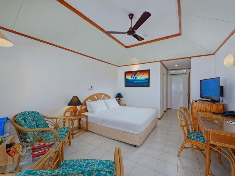 Helles Hotelzimmer mit Doppelbett, Deckenventilator und Sitzbereich mit Rattanmöbeln.