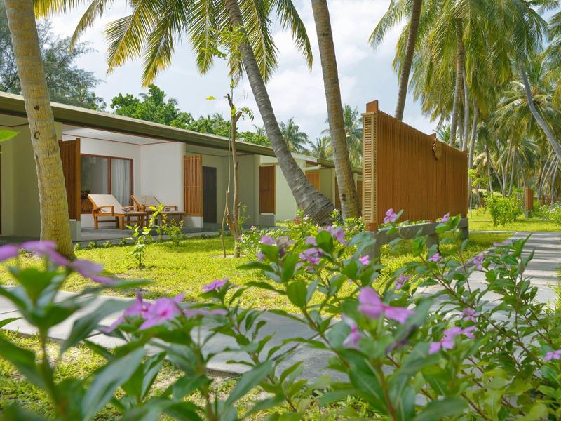 Moderne Bungalows mit Garten, Palmengras und blühenden Pflanzen an einem tropischen Urlaubsort.