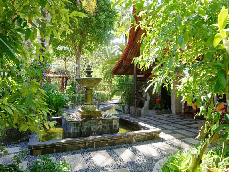Grüner Garten mit Springbrunnen und überdachtem Sitzbereich im Hintergrund
