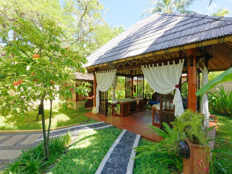 Offene Pavillon-Überdachung mit weißen Vorhängen im grünen Garten eines Resorts.