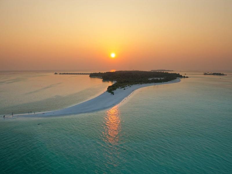 Sonnenuntergang über einer schmalen Sandbank, die sich ins ruhige Meer erstreckt.