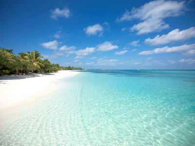 Weißer Sandstrand mit klarem, türkisfarbenem Wasser und blauem Himmel mit vereinzelten Wolken.